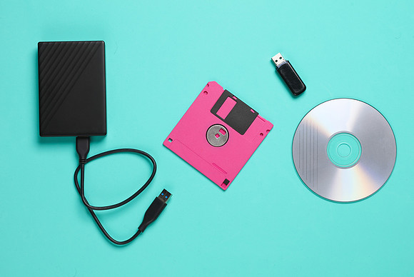 Floppy disks and cd drives, external hard drive and usb flash drive on blue background. Old and new storage technologies